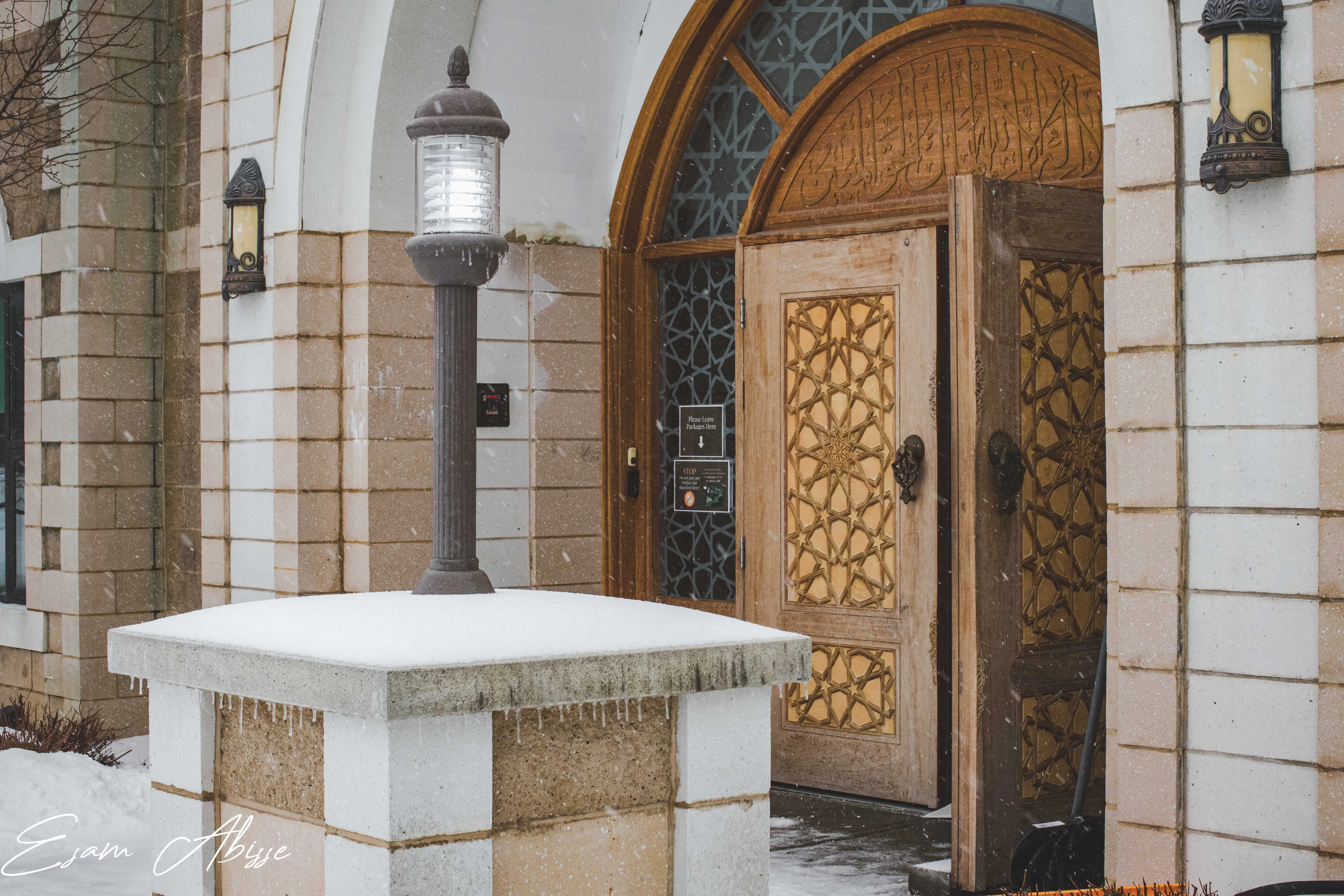 A snow-dusted mosque entrance with carved wooden doors during snowfall